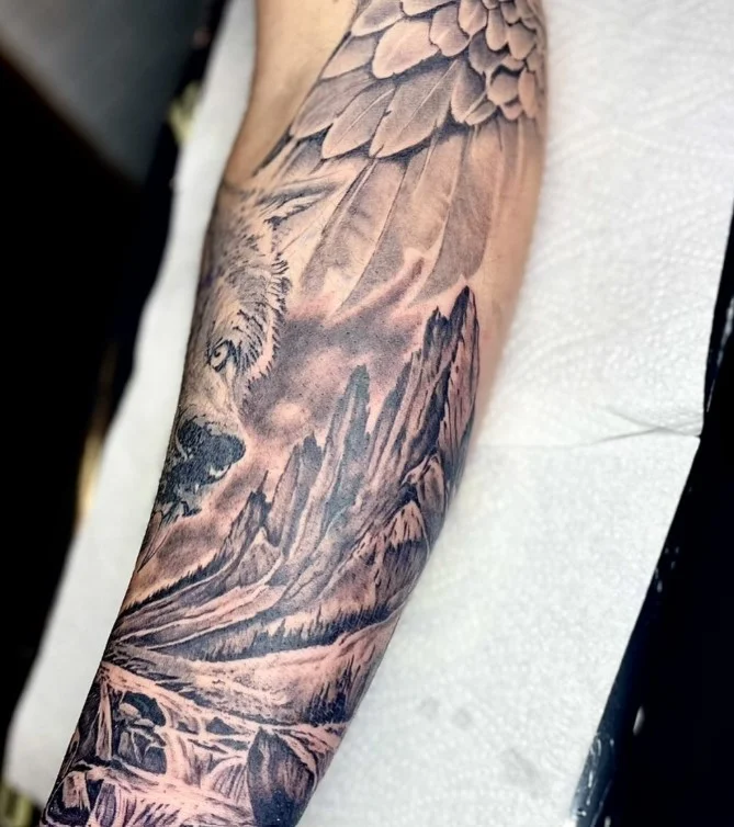 Mountain and nature scene wrap around arm tattoo with a scenic landscape design