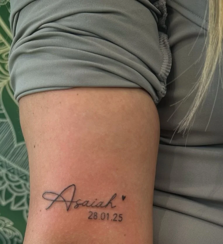 Minimal name and date forearm tattoo in clean decorative lettering