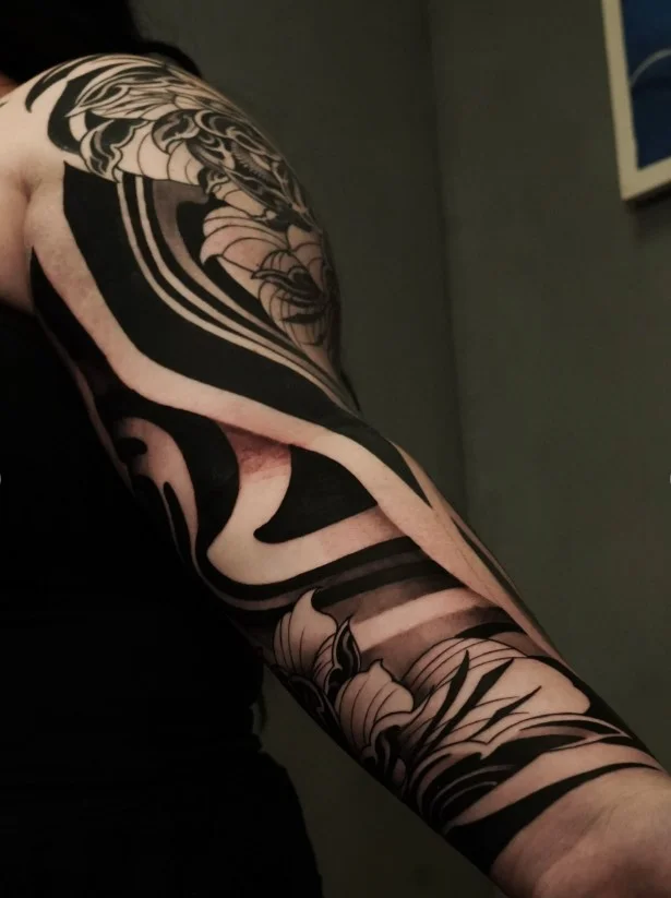 Ornamental floral blackwork wrap around arm tattoo with bold flowers and decorative details