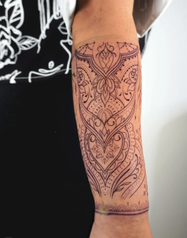 Ornamental mandala arm wrap tattoo with symmetrical decorative linework
