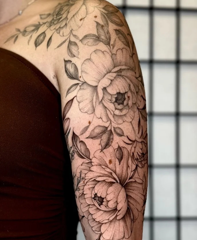 Peony upper arm tattoo with layered petals and feminine detailing