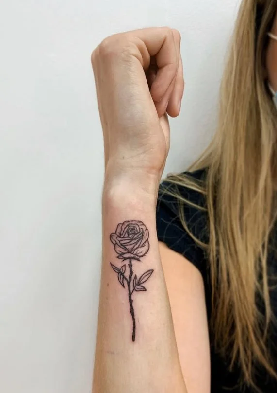 Detailed rose forearm tattoo with a long stem and realistic petal shading