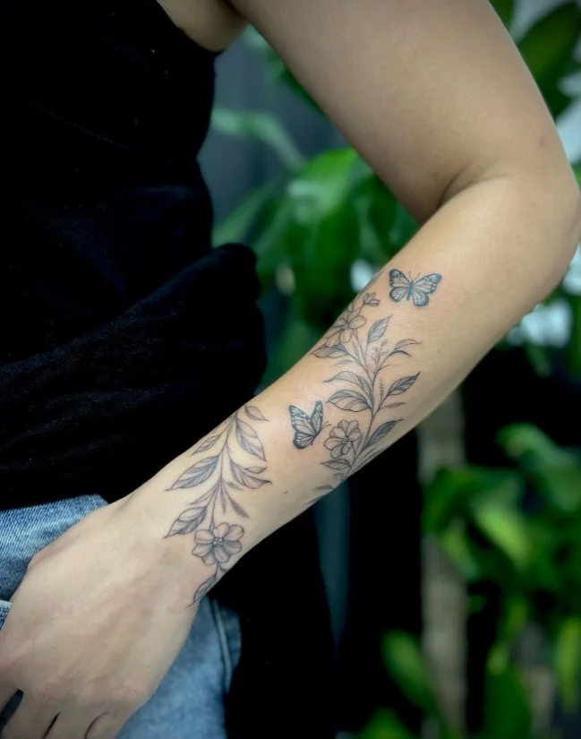 Detailed rose and leafy stems wrapping around a woman's forearm tattoo