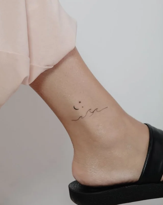 Minimal small ankle tattoo featuring a single flowing ocean wave line on the outer ankle