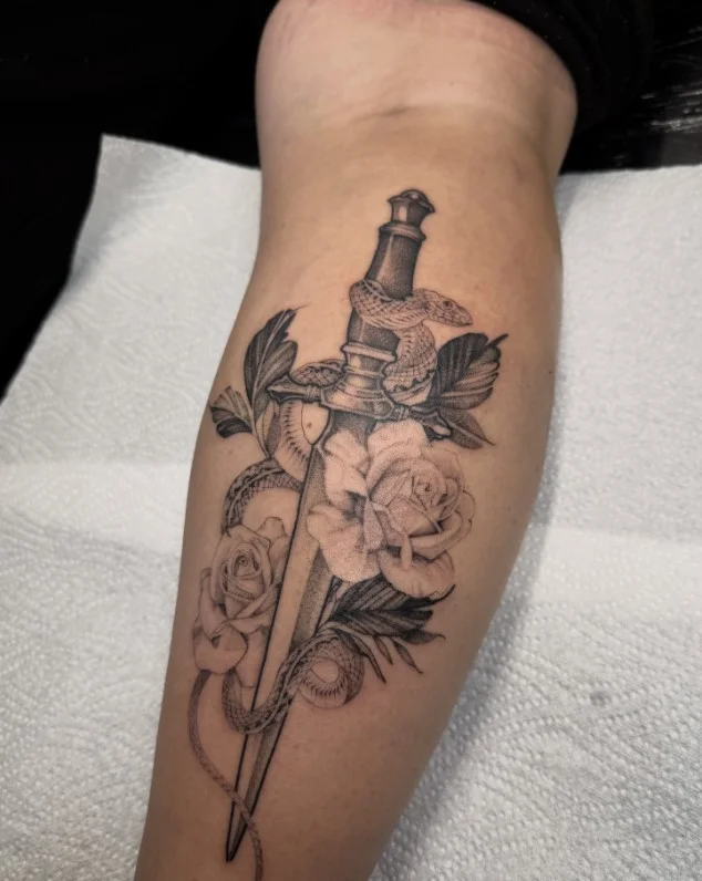Snake winding around a dagger in a calf tattoo for women
