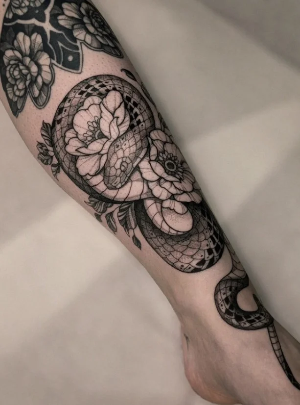 Snake and flower lower leg tattoo with a flowing vertical design