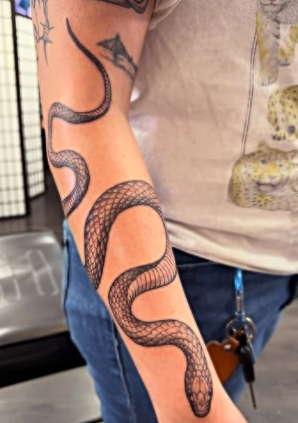 Curved snake forearm tattoo following the length of the arm with detailed scales