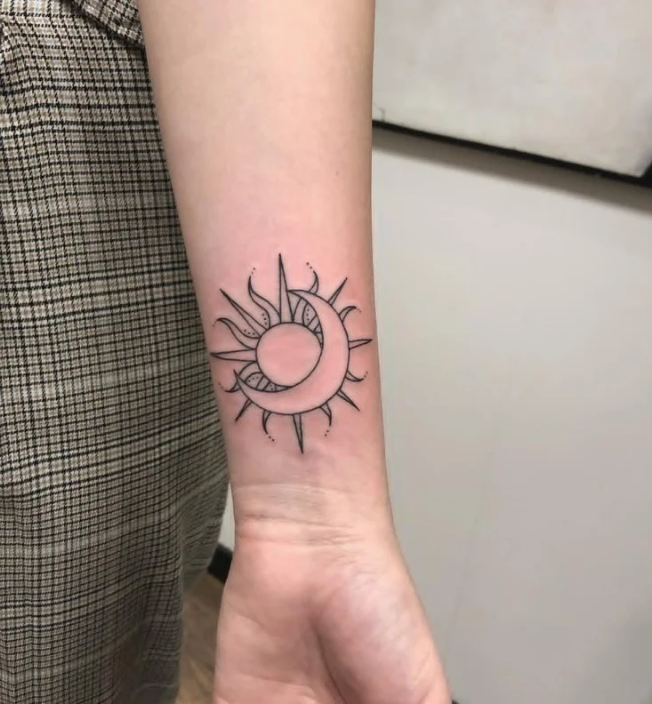 Sun and moon tattoo arranged as a balanced celestial design on the inner forearm