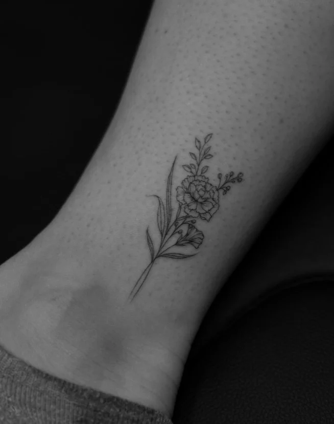 Small ankle tattoo featuring a delicate birth flower with a slender botanical stem above the ankle bone