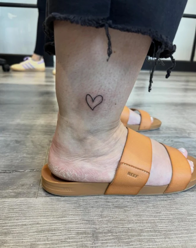 Small ankle tattoo featuring a simple heart outline placed delicately above the ankle bone