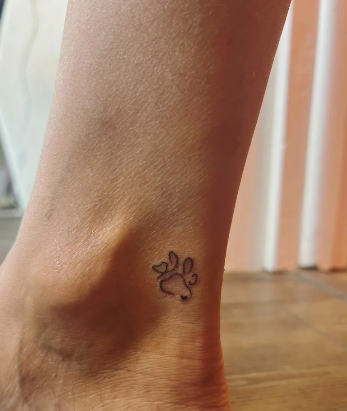 Small ankle tattoo featuring a minimalist paw print representing a beloved pet above the ankle