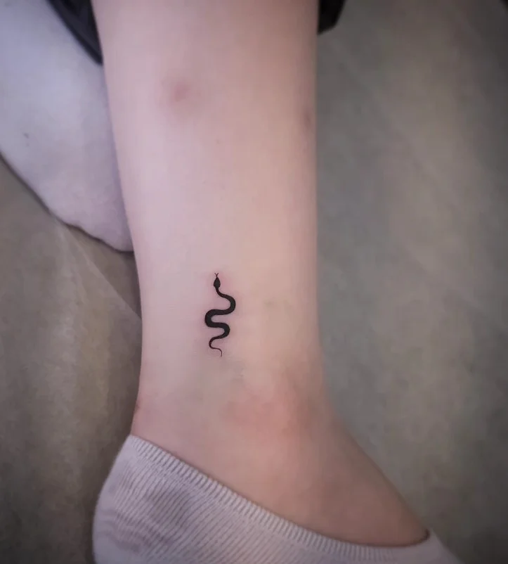 Small ankle tattoo featuring a slender minimalist snake curving naturally along the ankle