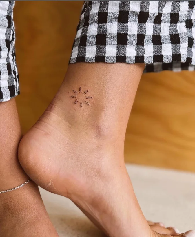 Small ankle tattoo featuring a simple outlined sun with evenly spaced rays above the ankle bone
