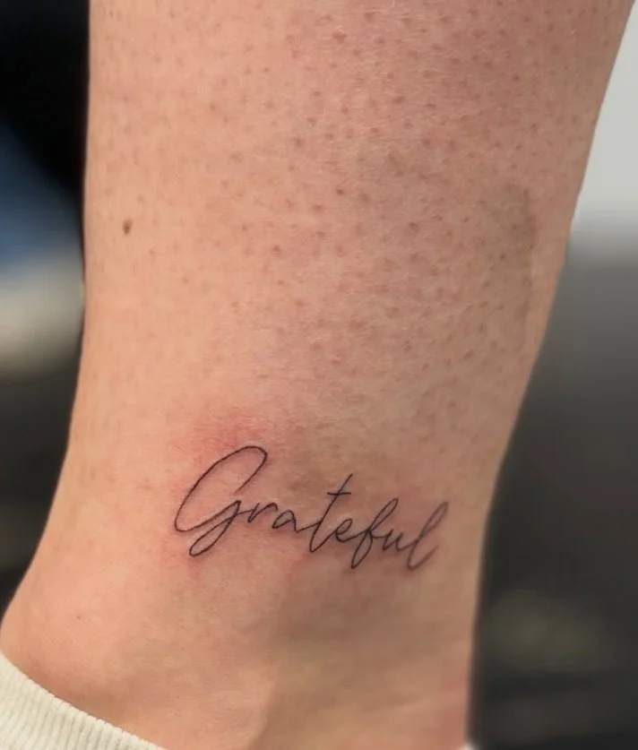 Small ankle tattoo featuring a short meaningful word in delicate minimalist lettering on the inner ankle
