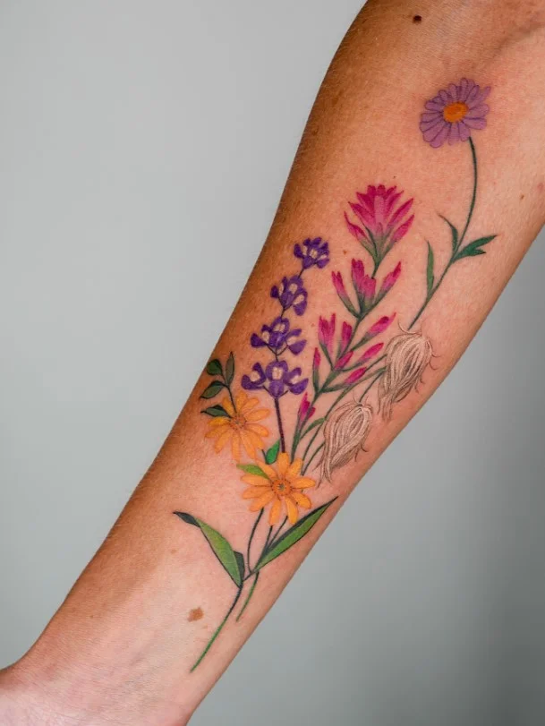 Wildflower bouquet forearm tattoo featuring several delicate blooms and leafy stems