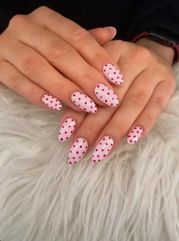 Baby pink manicure with evenly spaced cherry-red polka dots on glossy oval nails.