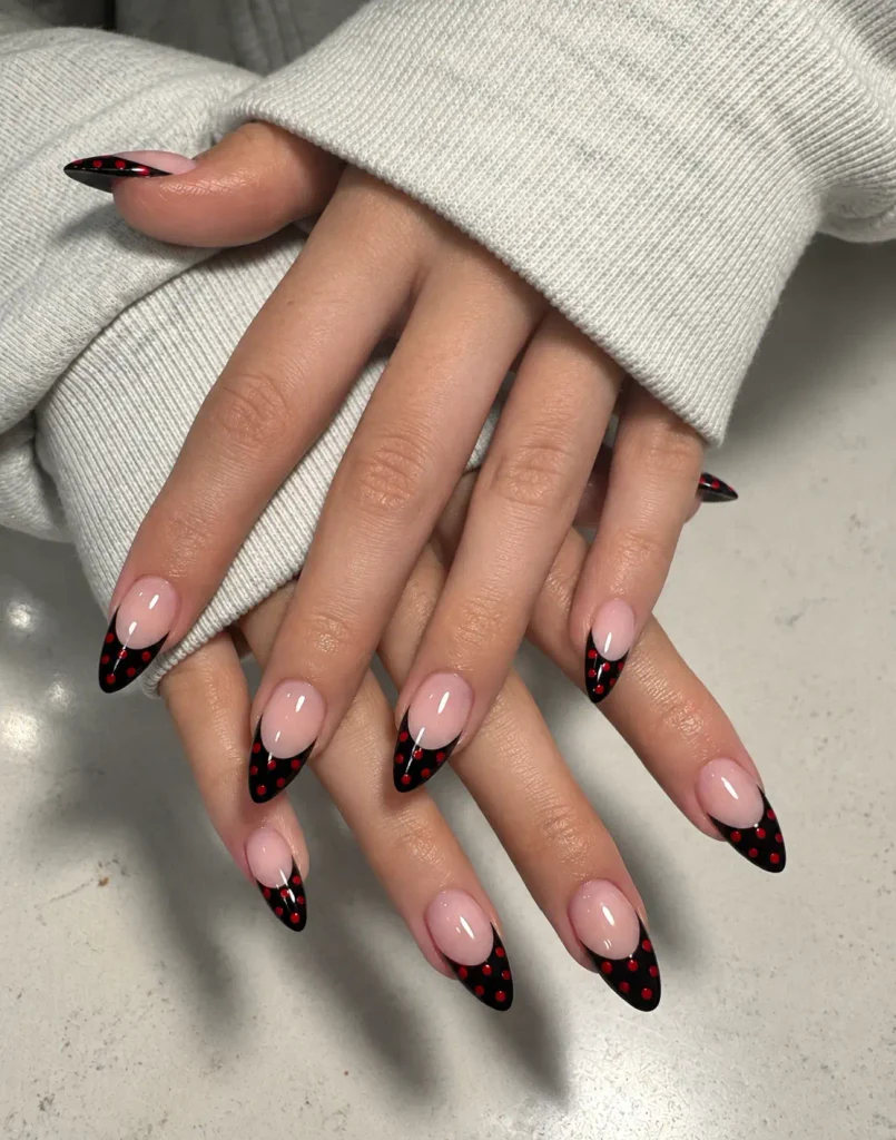 Black French tip nails with small red polka dots on a sheer nude base