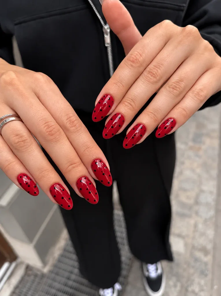 Cherry-red nails decorated with tiny black polka dots on short square nails