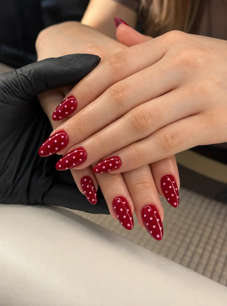 Glossy cherry-red manicure featuring contrasting pale pink polka dots.