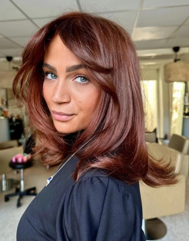 Copper red hair with warm red-orange tones styled in soft waves, illustrating a vibrant hair color against pale skin and blue eyes.