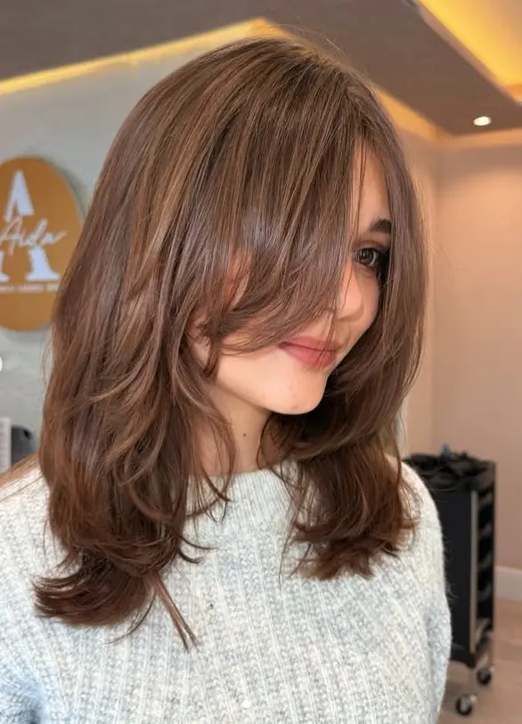 Woman with dark brown shoulder-length hair, soft curtain bangs, and face-framing layers