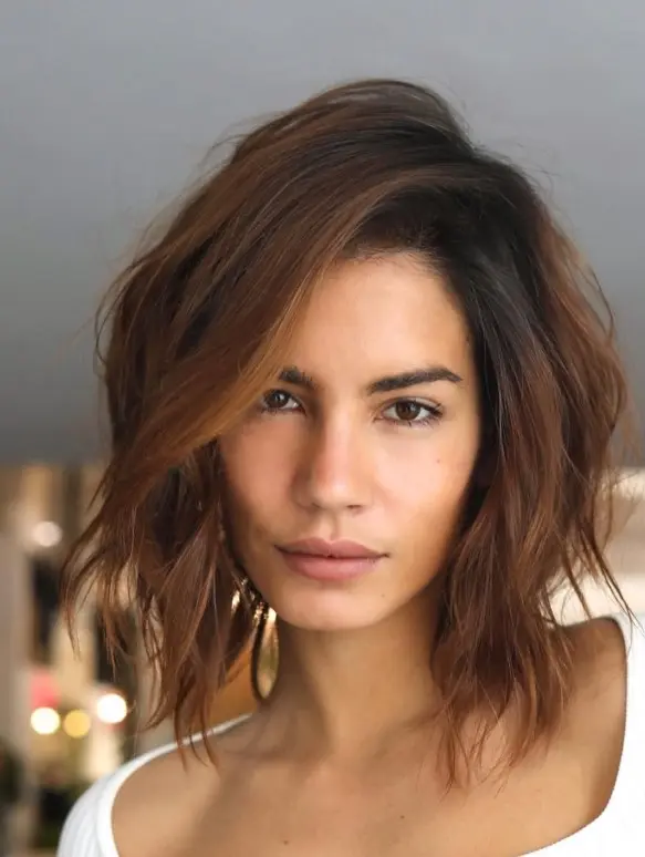 Dark brown shoulder-length hair styled with a deep side part and lifted roots