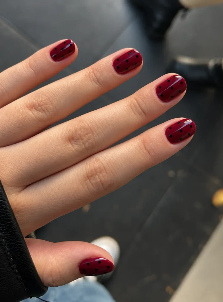 Deep burgundy nails with small black polka dots and a glossy finish