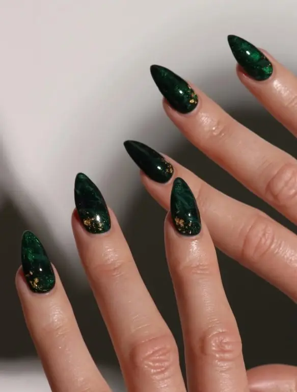 Glossy deep emerald green Christmas nails with irregular reflective gold foil flakes on accent nails