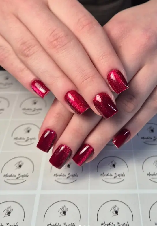 Short deep red velvet cat-eye Christmas nails with a glowing magnetic shimmer finish.