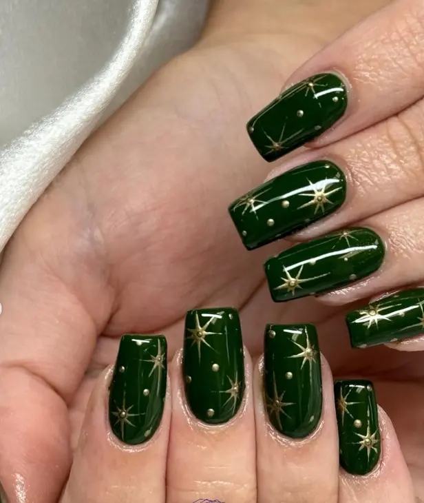 Emerald green Christmas nails with tiny gold stars and starburst accents scattered across selected nails