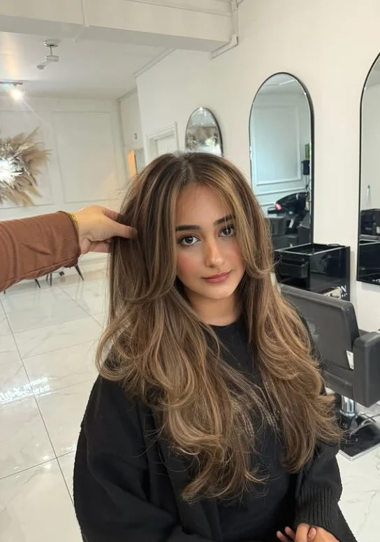 Honey blonde balayage on light olive skin with golden highlights blended into a brunette base.