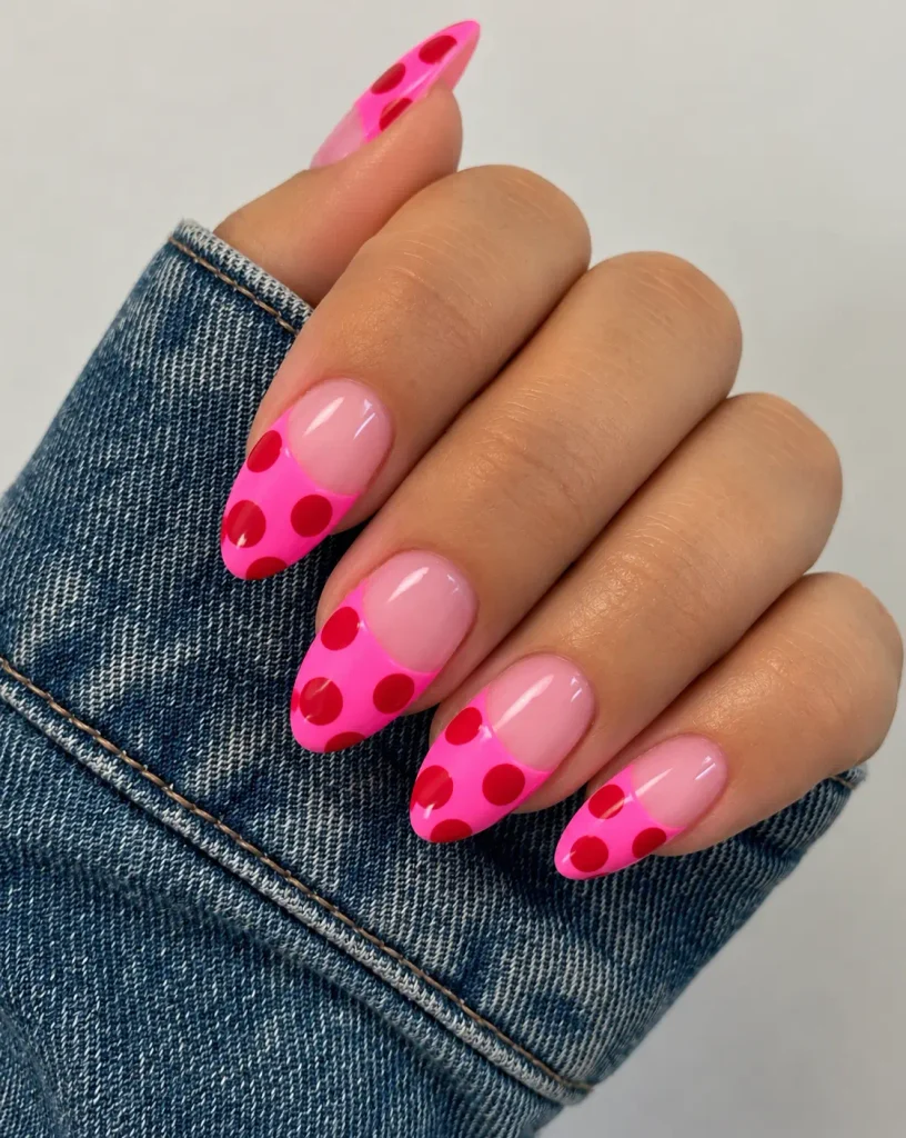 Bright hot-pink nails with large cherry-red polka dots spaced across each nail.