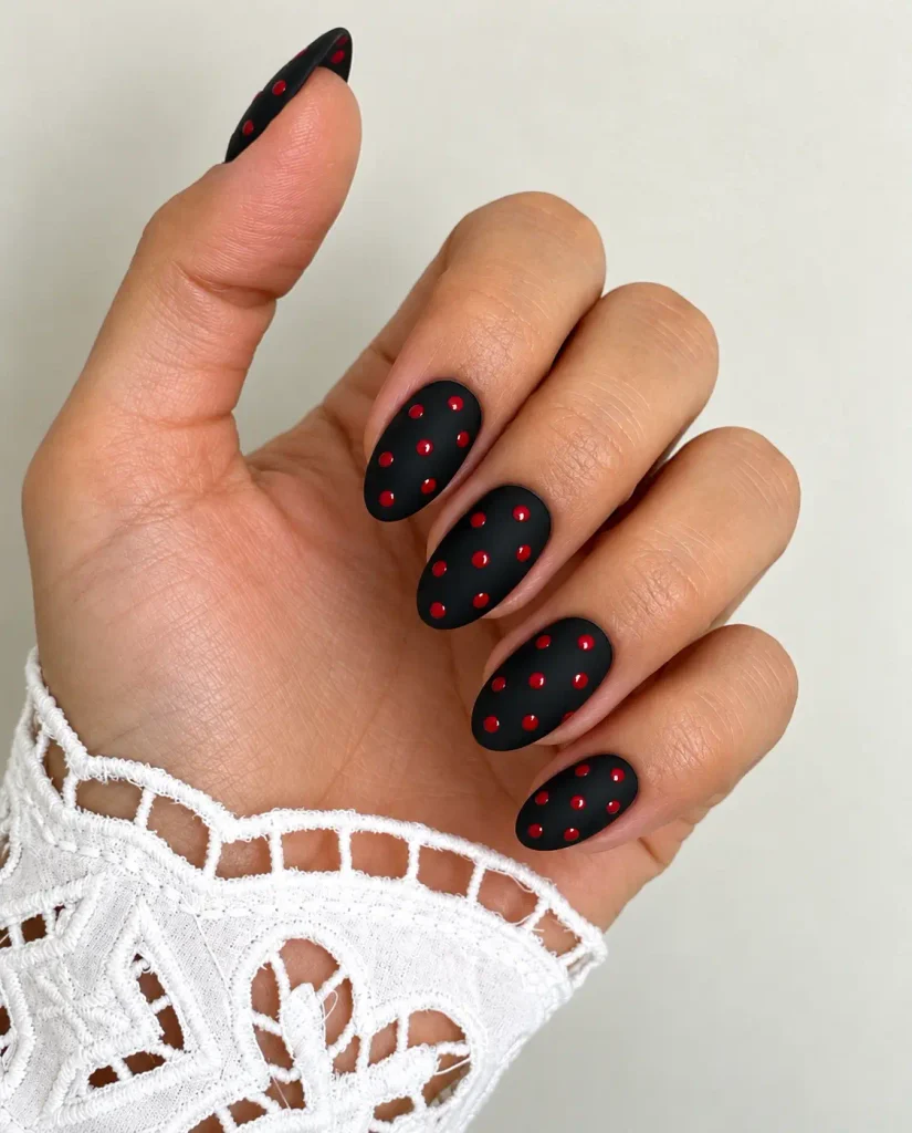 Matte black nails with glossy red polka dots for a contrasting finish
