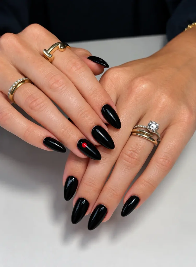 Minimalist glossy black nails with one small red dot near each cuticle