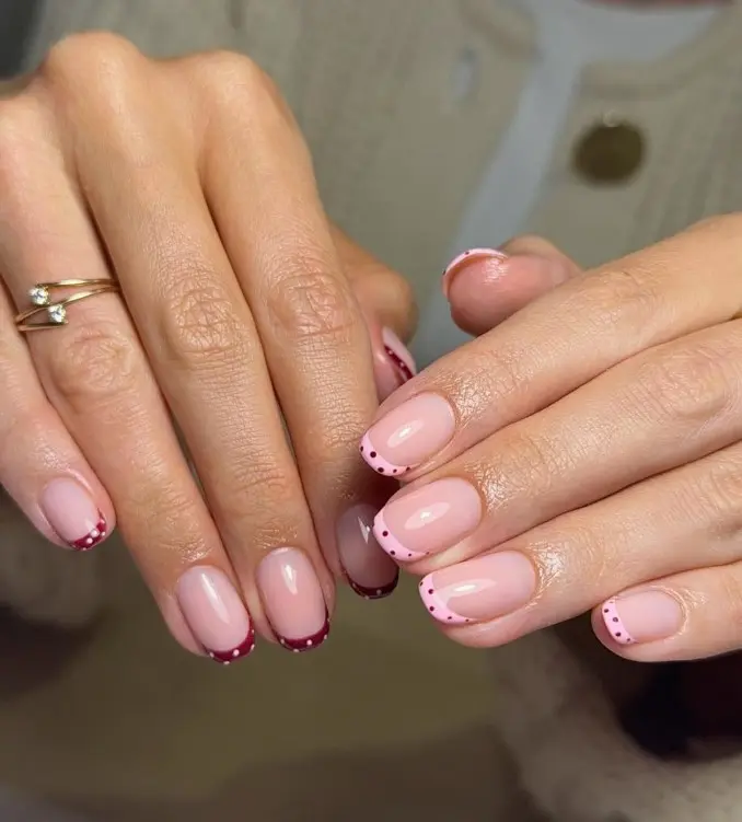 Pale pink French manicure with cherry-red tips decorated with small pink dots.
