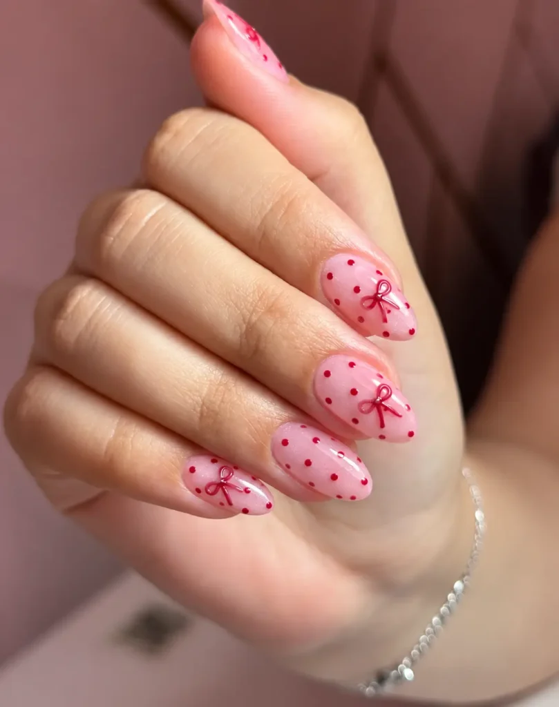 Pink nails with small red polka dots and a delicate red bow accent.