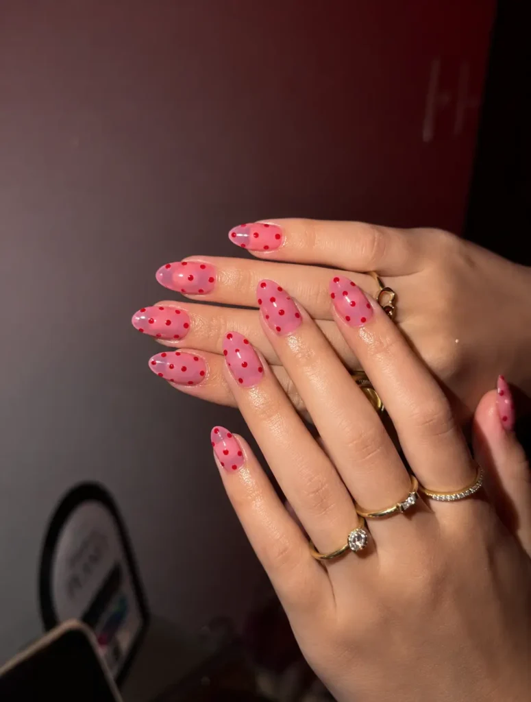 Translucent jelly-pink nails with bright red polka dots and a glossy finish.