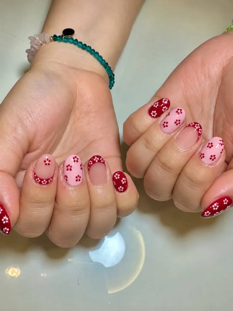 Pale pink nails decorated with small flowers made from red nail-polish dots.