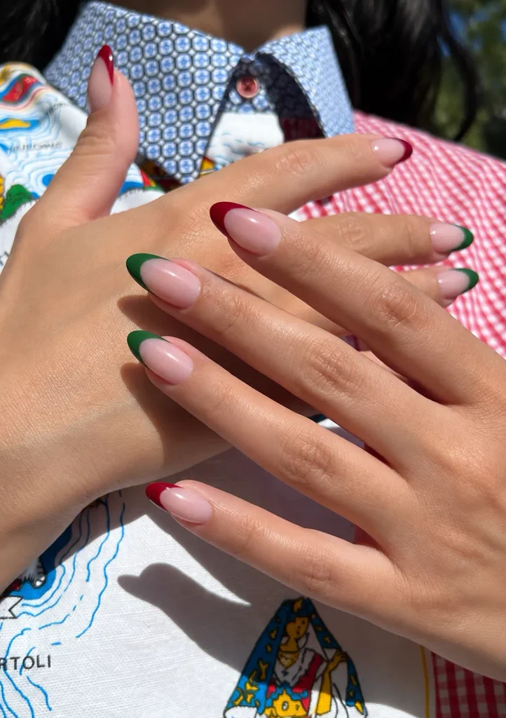 Red and green Christmas French tip nails with alternating colored tips on a sheer nude pink base