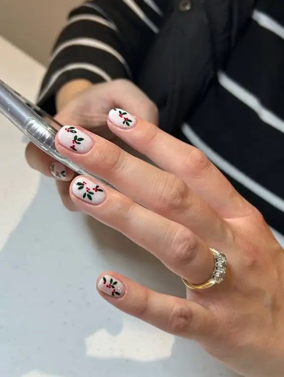 Christmas nails with green holly leaves and red berries painted on a milky white base
