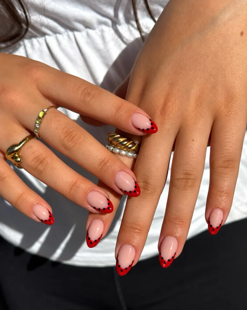 Cherry-red French tip nails with tiny black dots along the curved edges