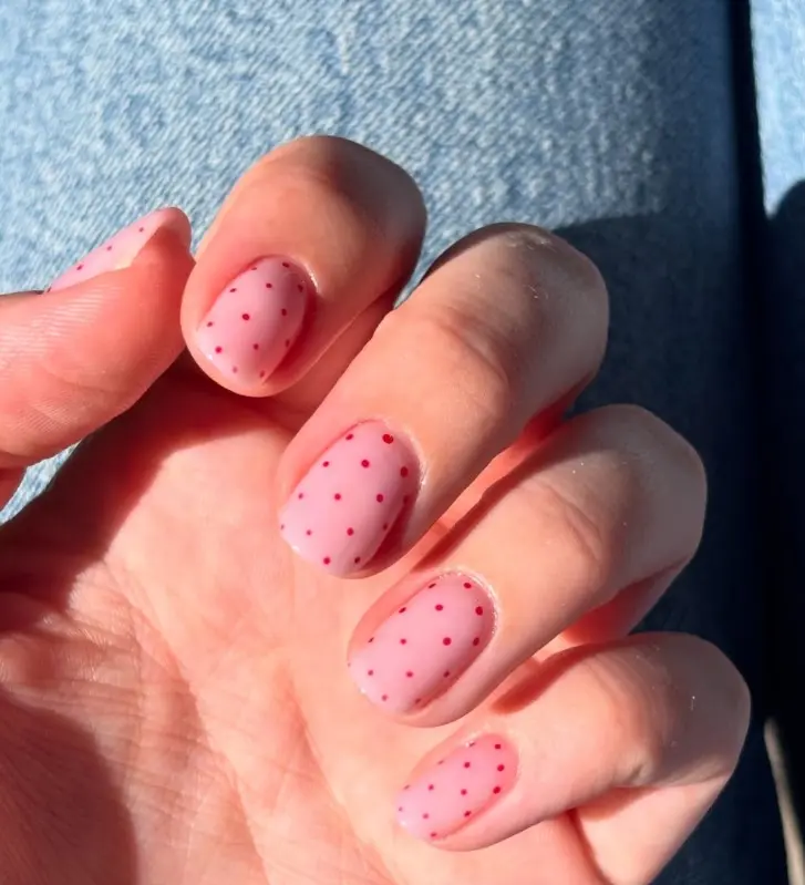 Sheer pink nails decorated with tiny red dots in a delicate scattered pattern.