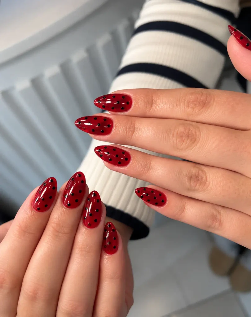 Sheer red jelly nails with crisp black polka dots and a translucent finish