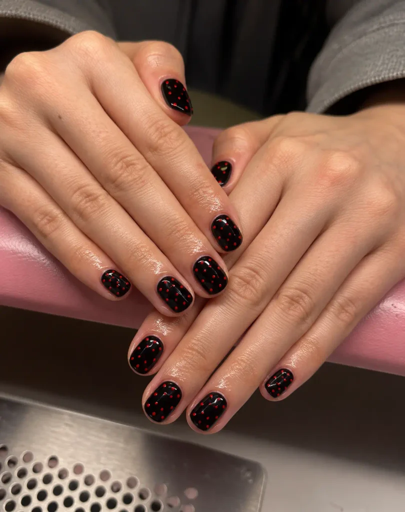 Short black nails decorated with tiny red micro-dots in a delicate pattern