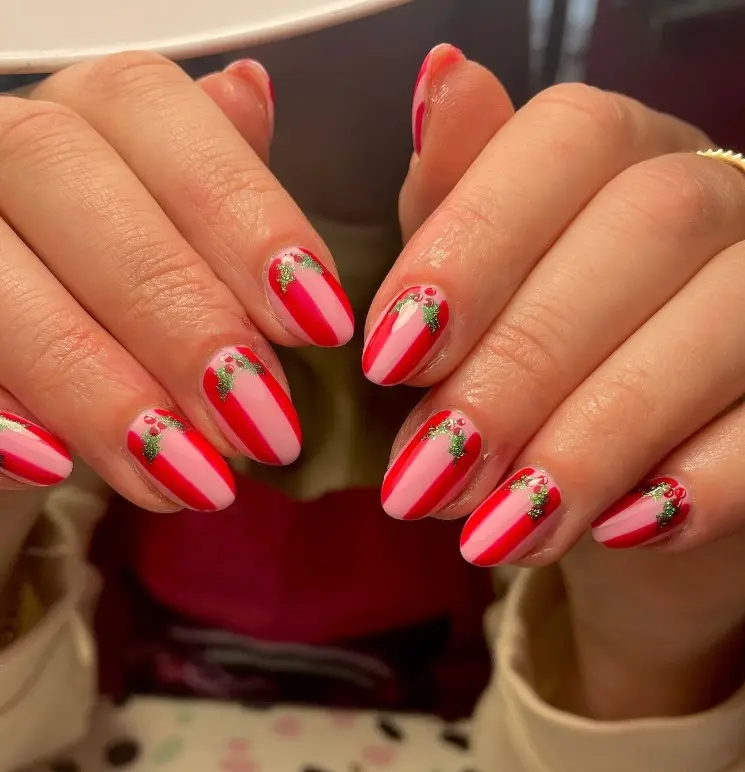 Short red Christmas nails featuring tiny green holly leaves and red berry nail art.