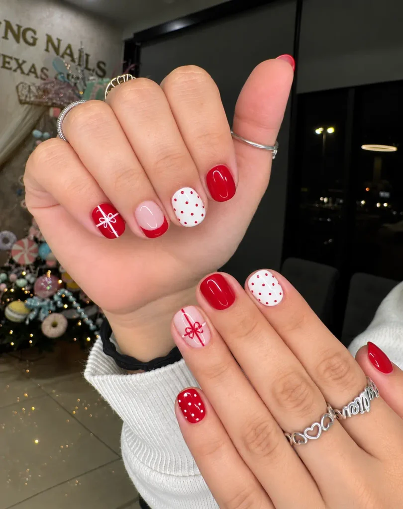 Short red Christmas nails with thin white gift-wrap ribbon lines and a small bow accent.