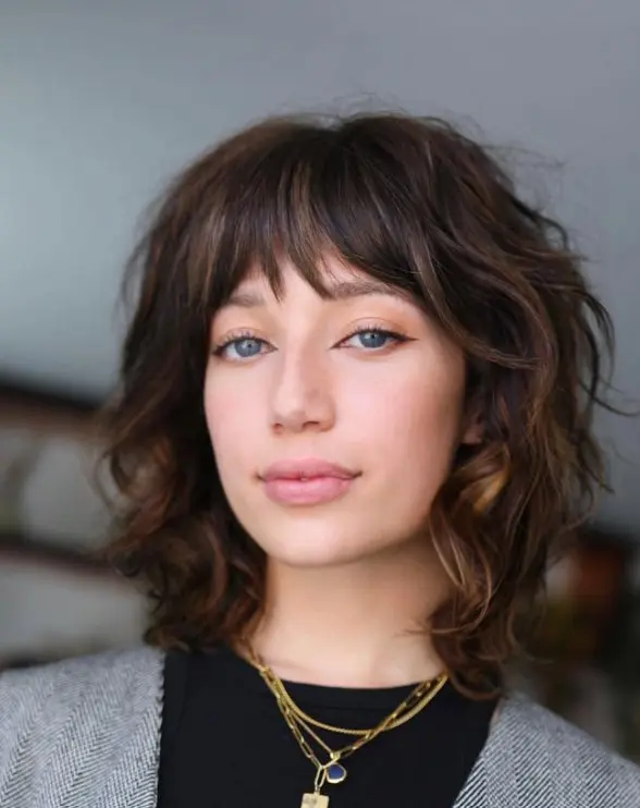 Woman with a textured dark brown shoulder-length shag haircut and wispy bangs